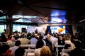 Audience members sitting at tables photographed from behind at the AI in Action Business Summit.